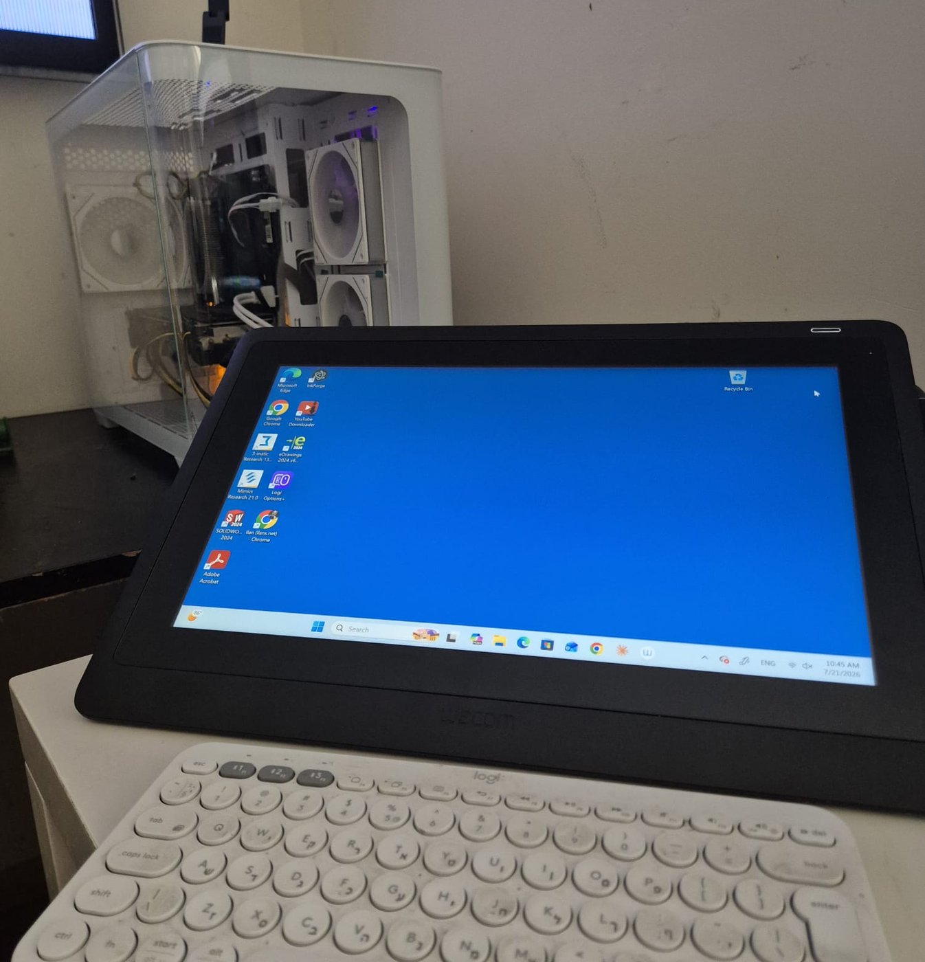 The actual machine: a compact white PC tower with visible fans, next to a pen display and compact keyboard on a small desk